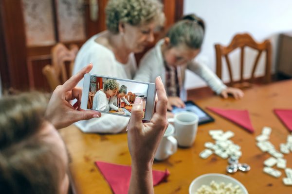 Grandmother and granddaughter play a game on the tablet while the mother takes a photo with the smartphone. Selective focus on smartphone in foreground